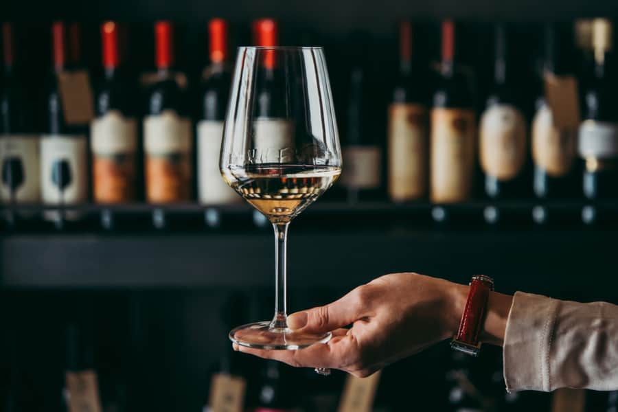 Hand Holding A White Wine Glass In A Restaurant Setting.